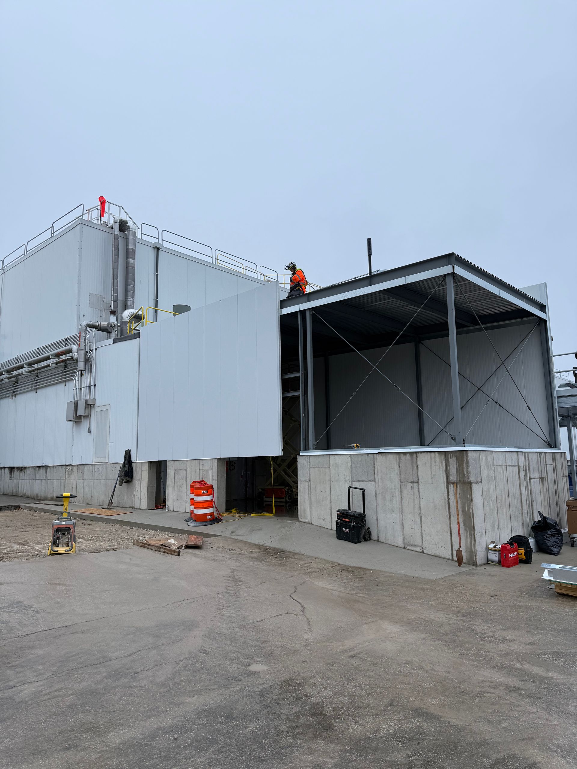 Construction site. Workers on building roof and metal frame structure. Concrete blocks and gray exterior.