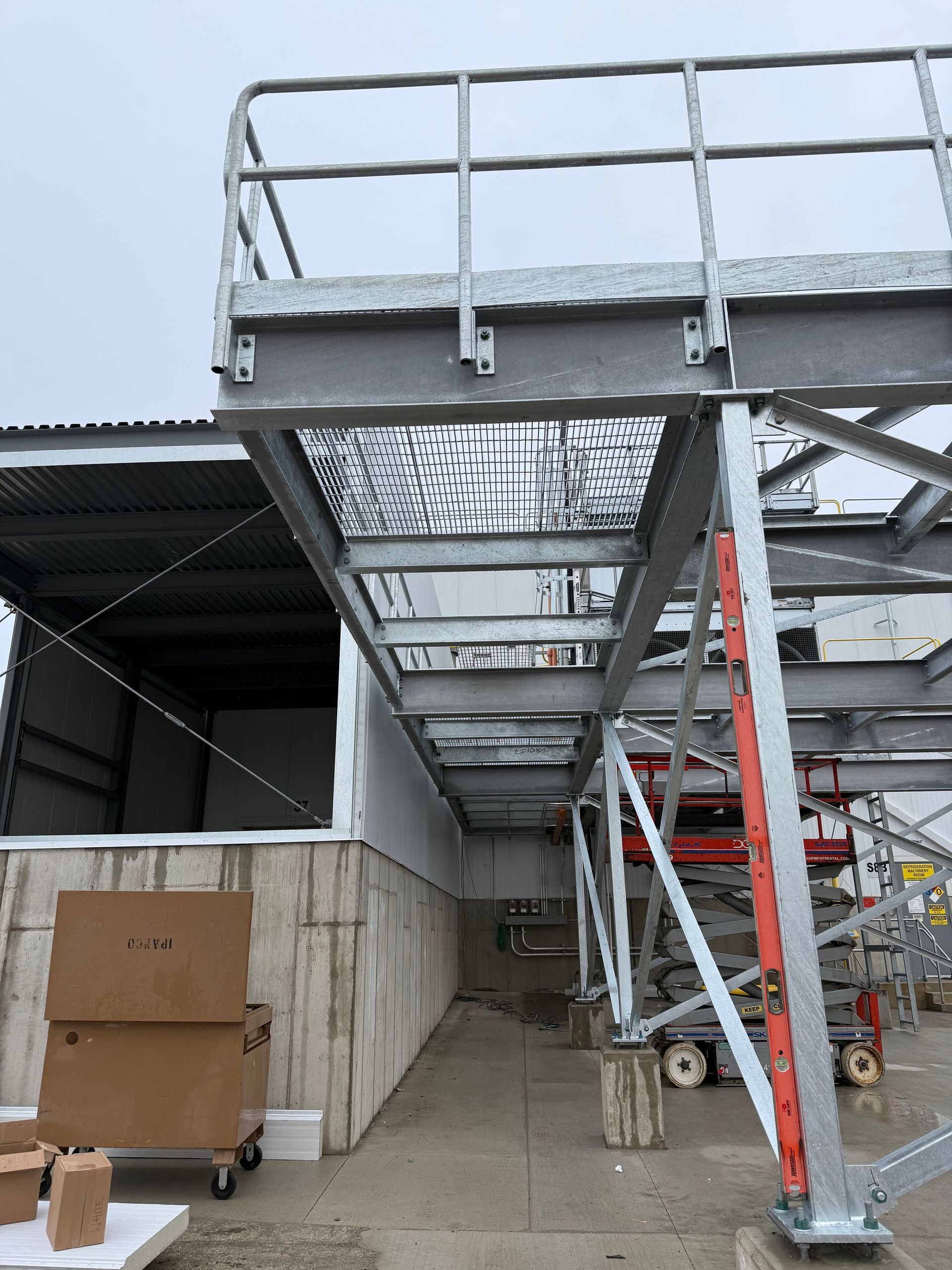 Metal platform with grating and guardrails attached to a building, supported by scaffolding.
