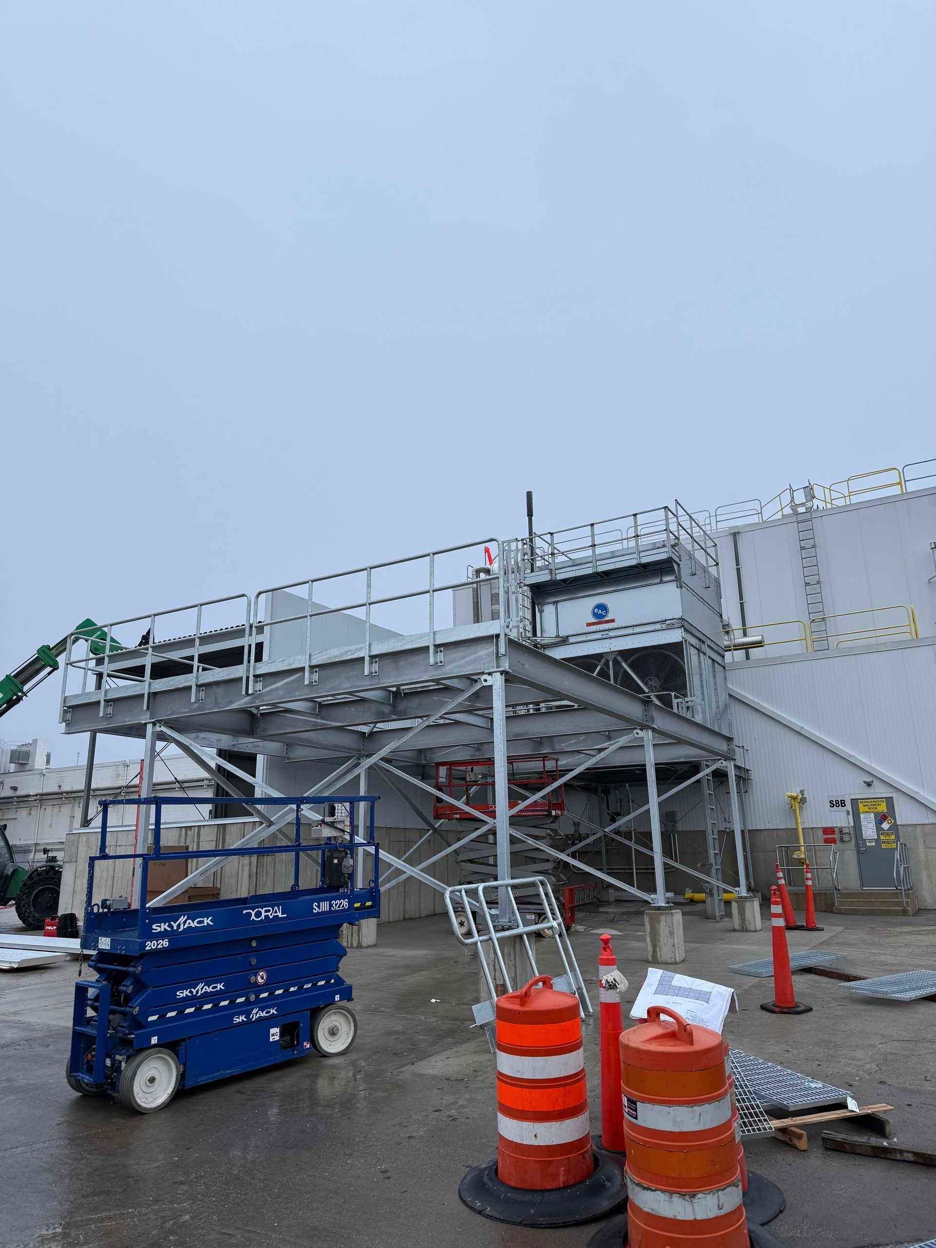 Blue scissor lift near a steel scaffolding structure attached to a building, with construction cones in front.