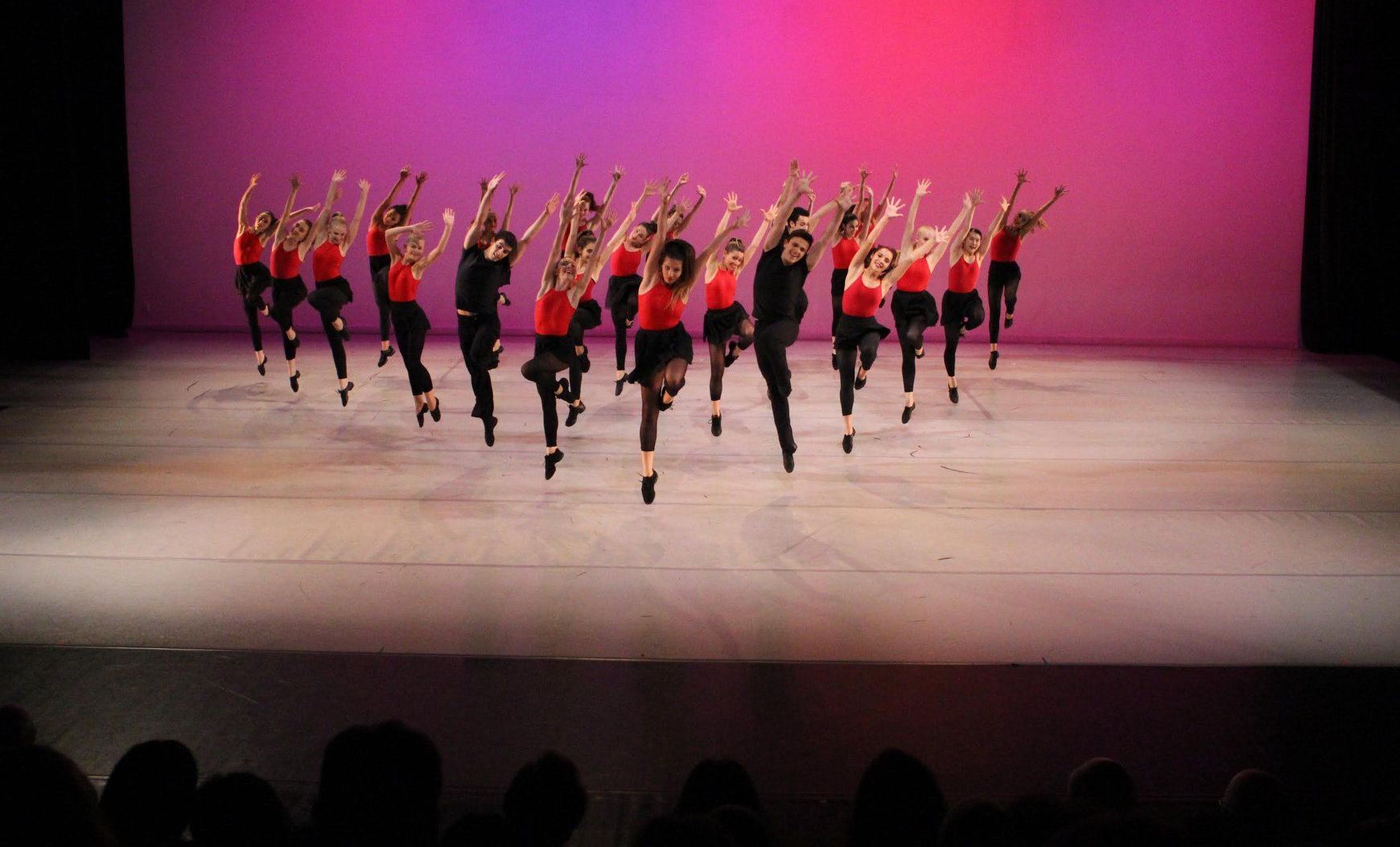 A group of people are dancing on a stage with a pink background