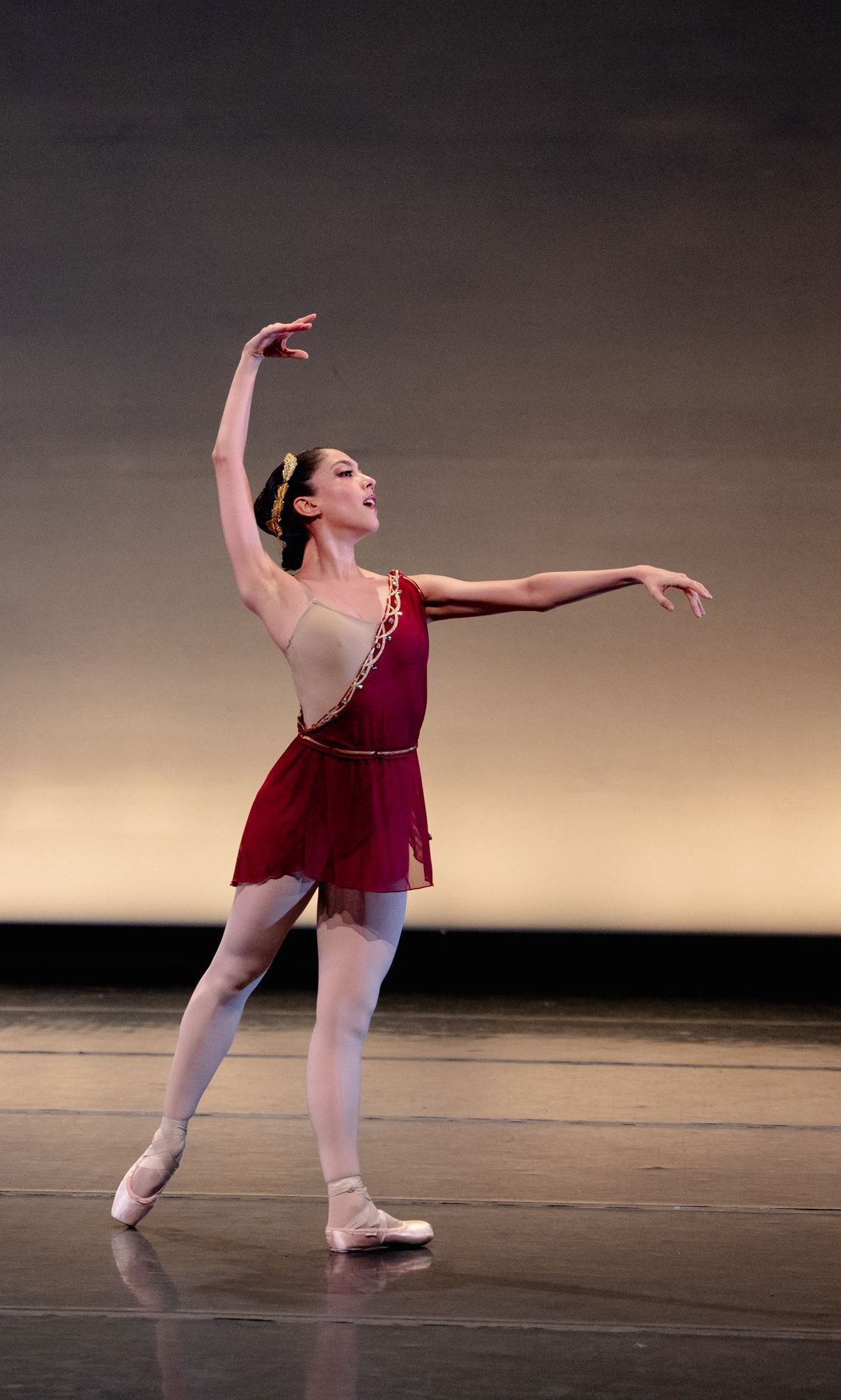 A ballerina in a red dress is dancing on a stage.