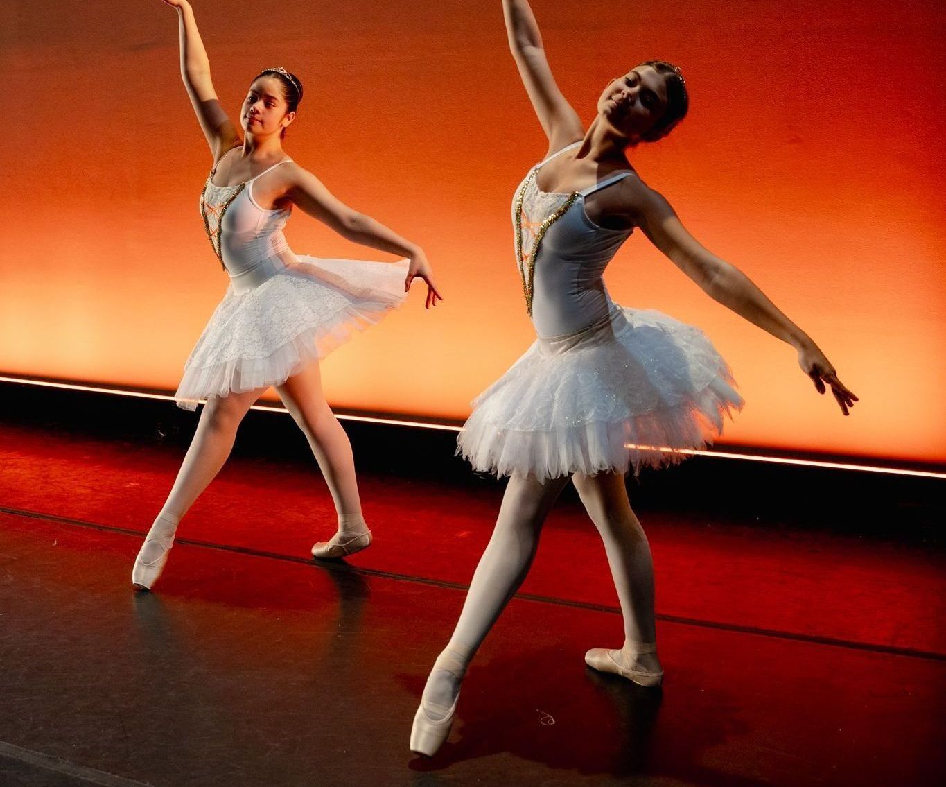 Two ballerinas in white tutus are dancing on a stage