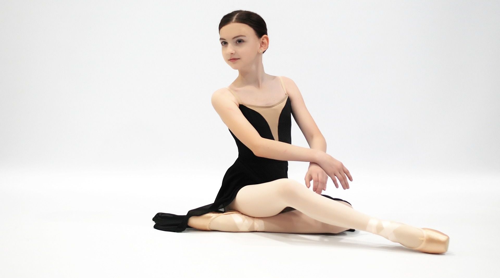 A young ballerina is sitting on the floor wearing pointe shoes.