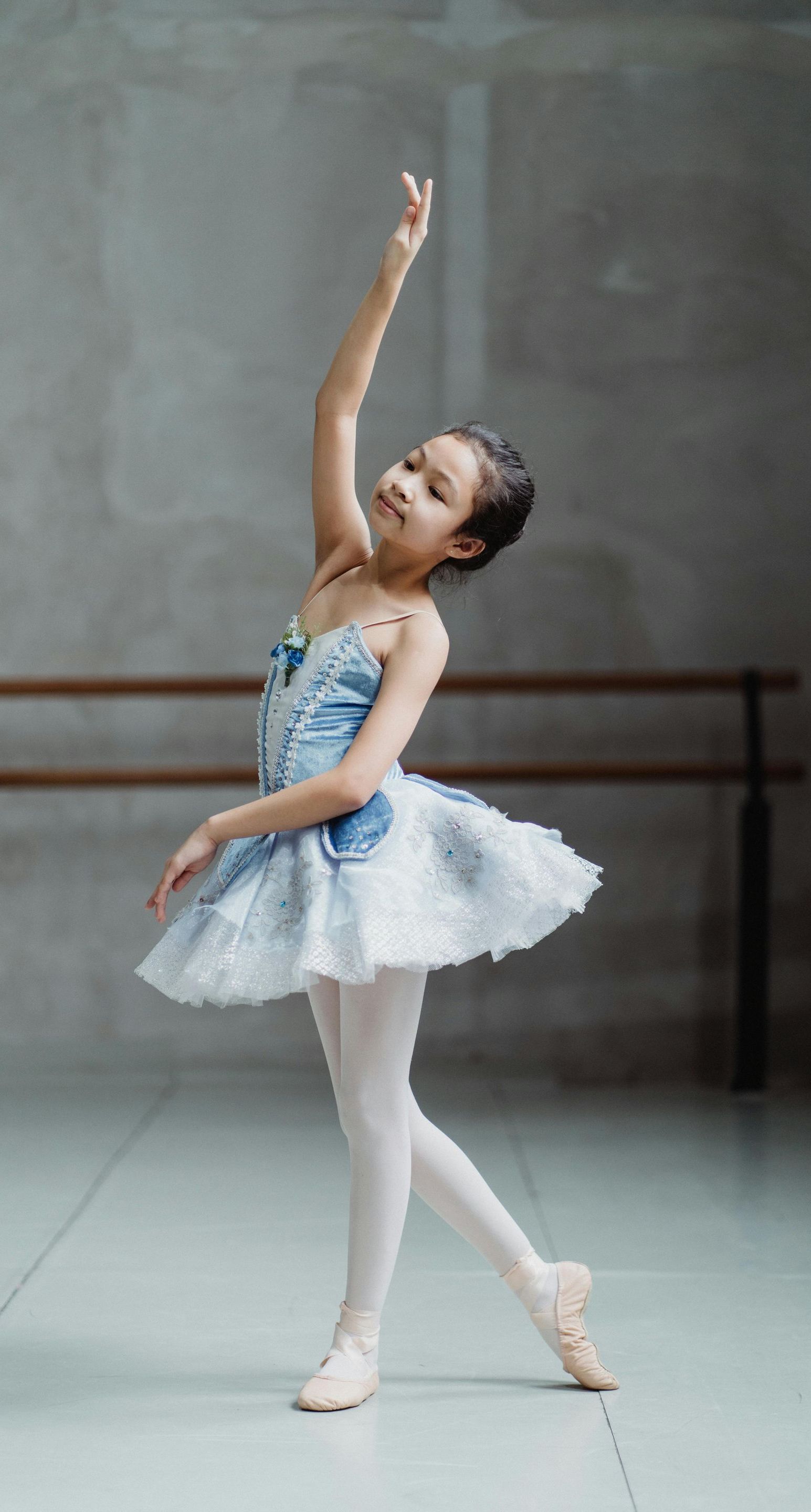 A little girl in a blue and white tutu is dancing in a dance studio.