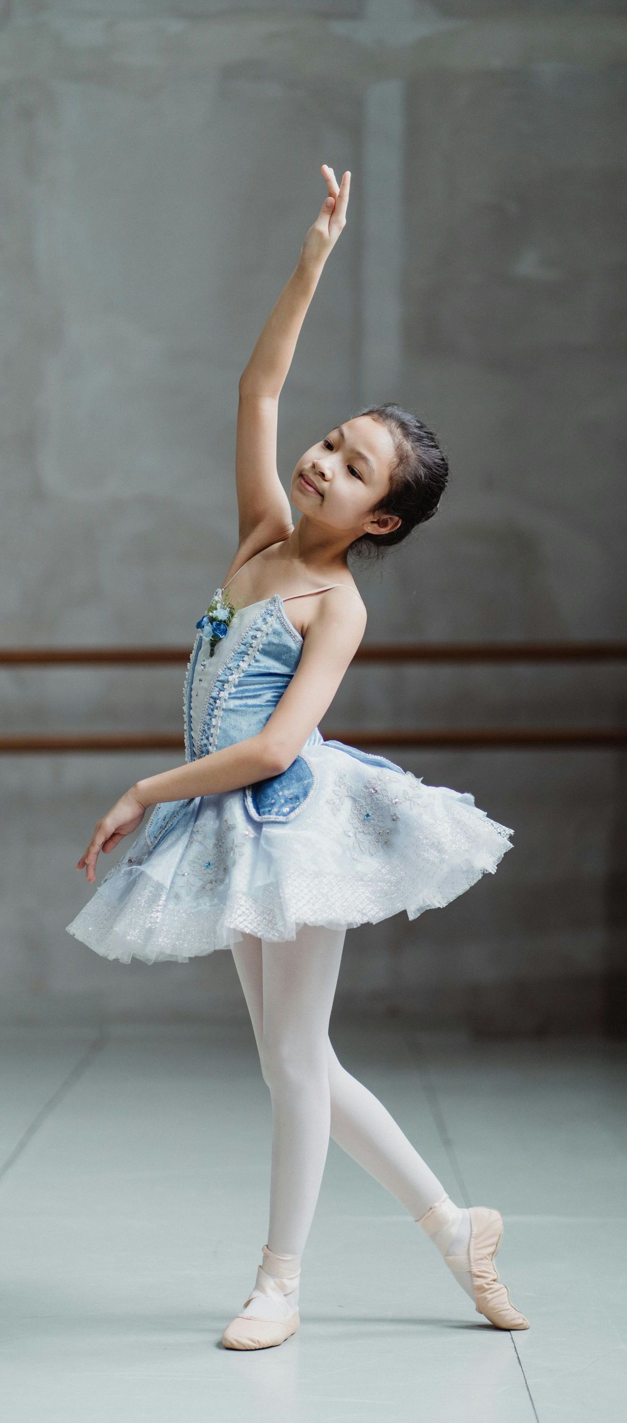 A young girl in a blue and white tutu is dancing in a dance studio.