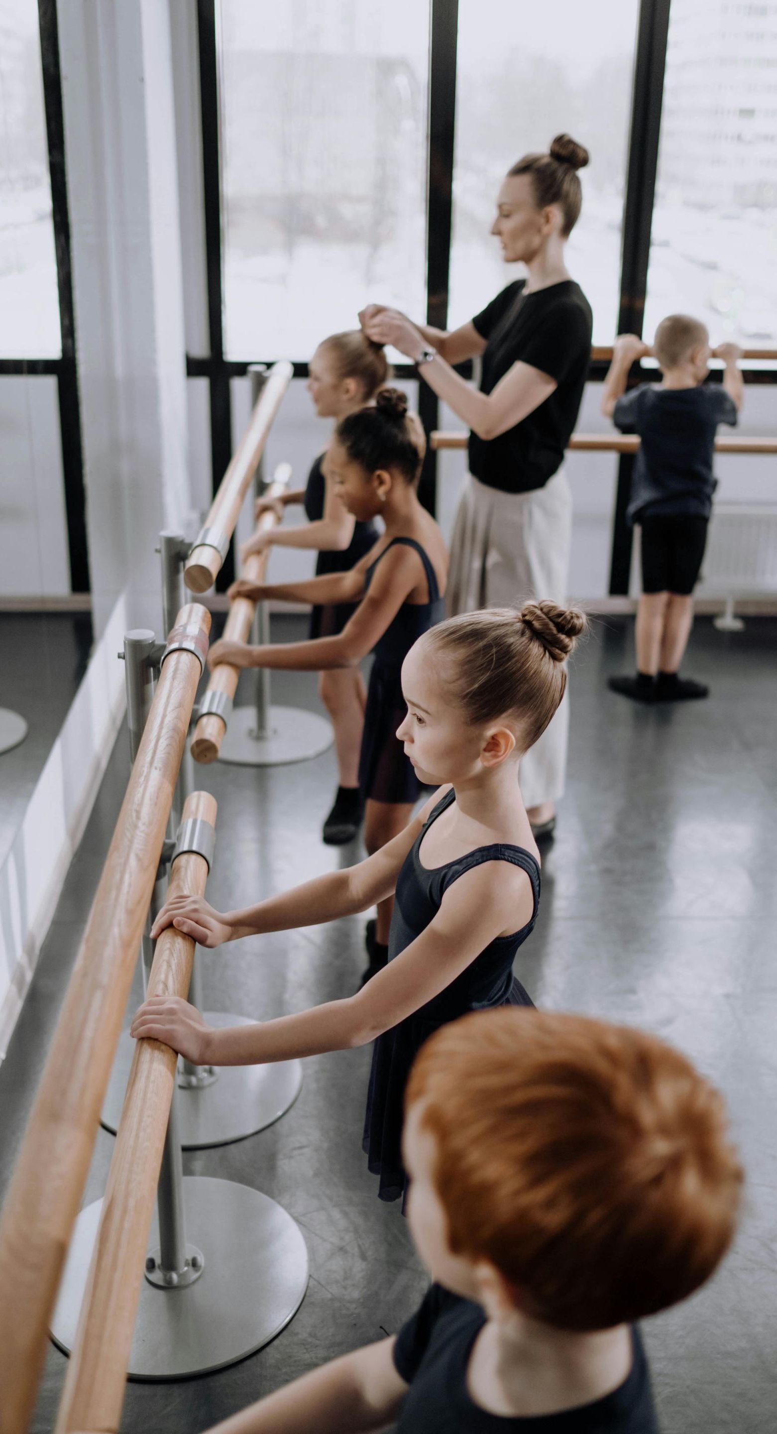 A group of young ballerinas are practicing at a barre in a dance studio.