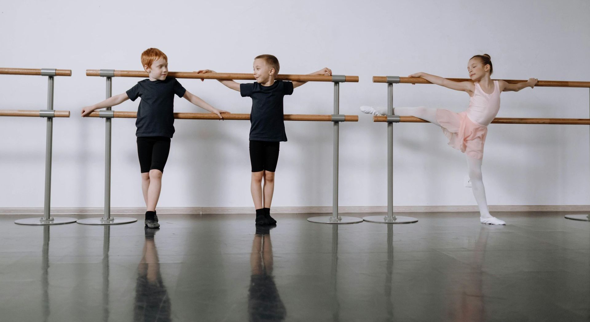 Three children are practicing ballet in a dance studio.