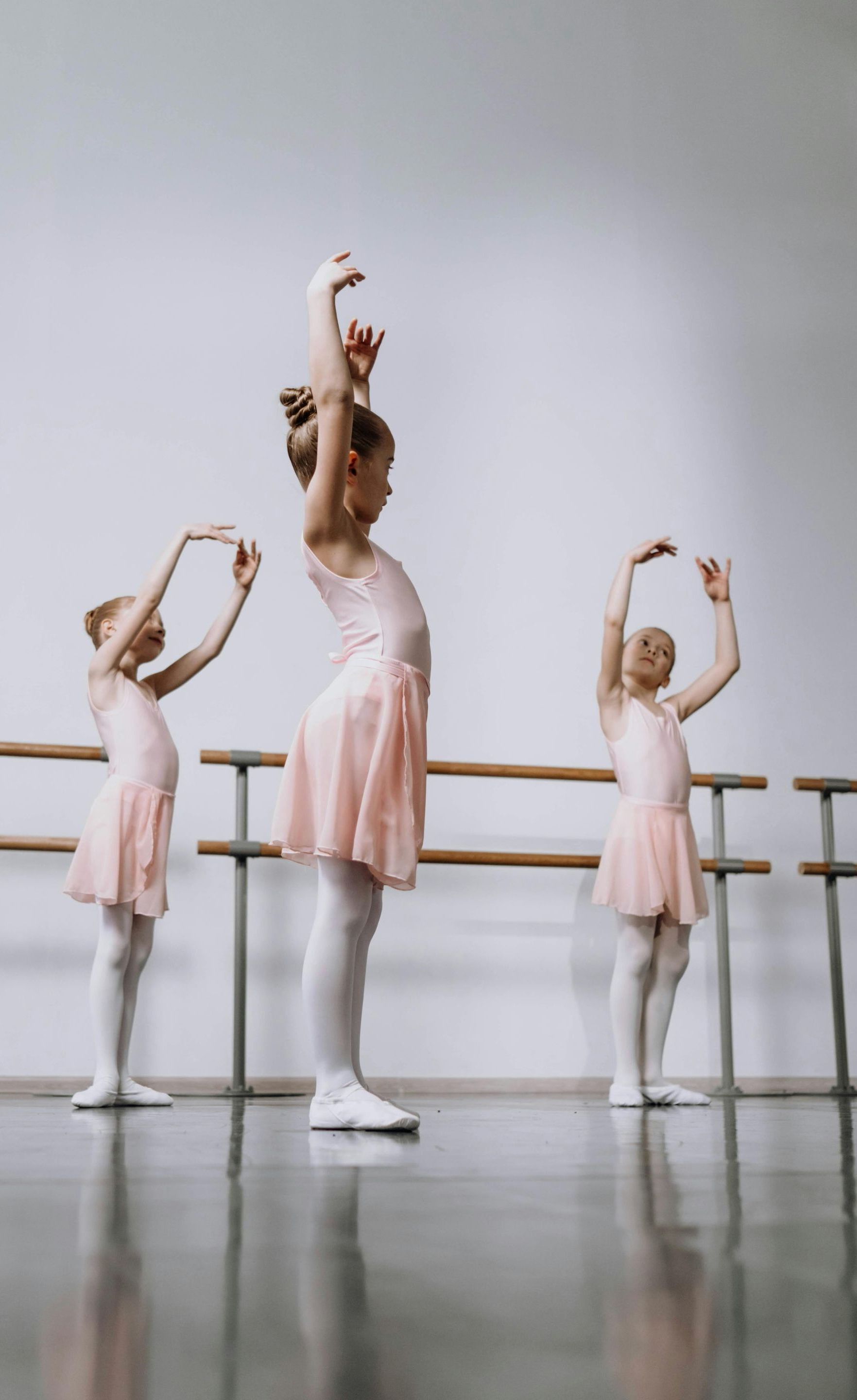 Three little girls are practicing ballet in a dance studio.