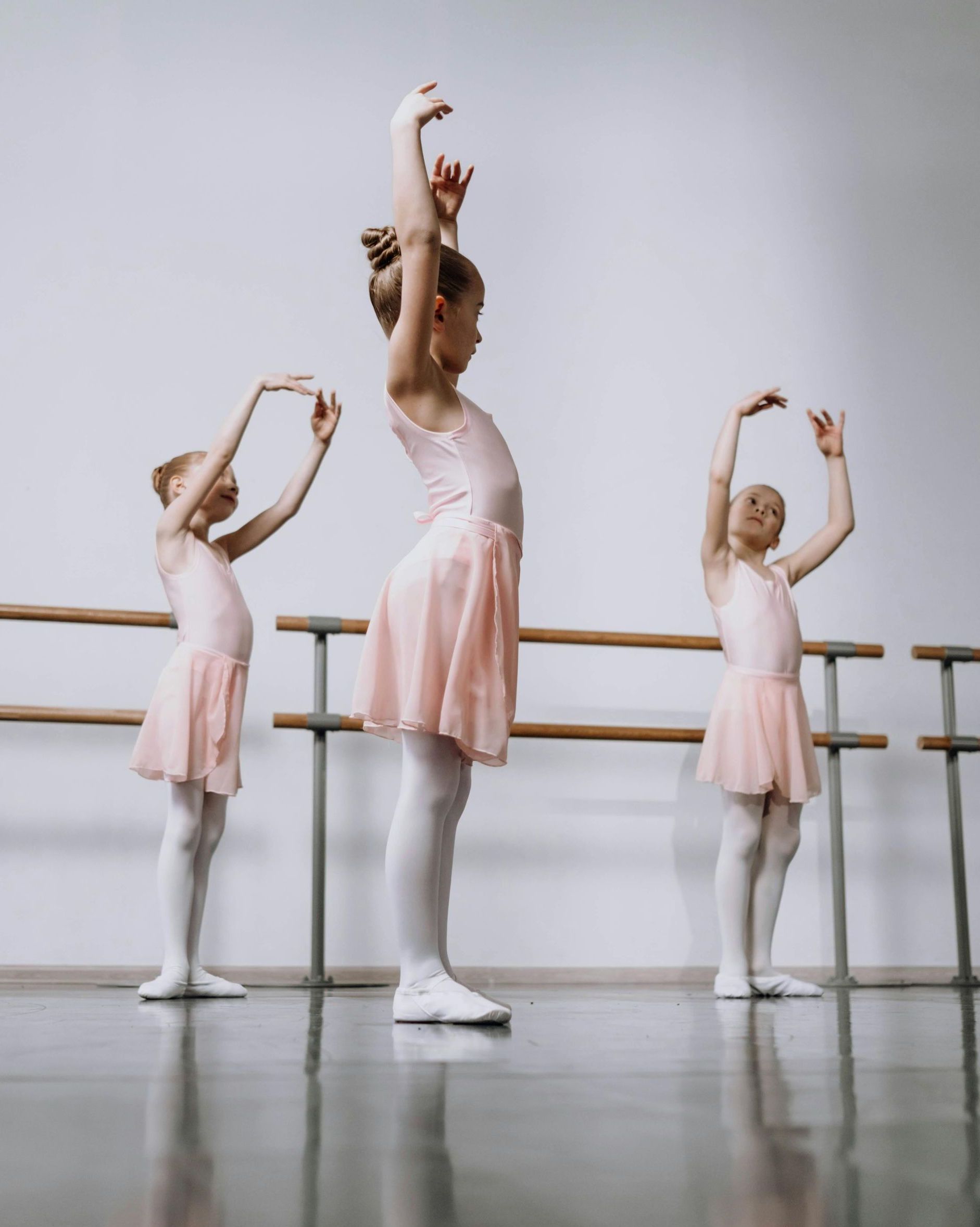 Three young girls are practicing ballet in a dance studio.