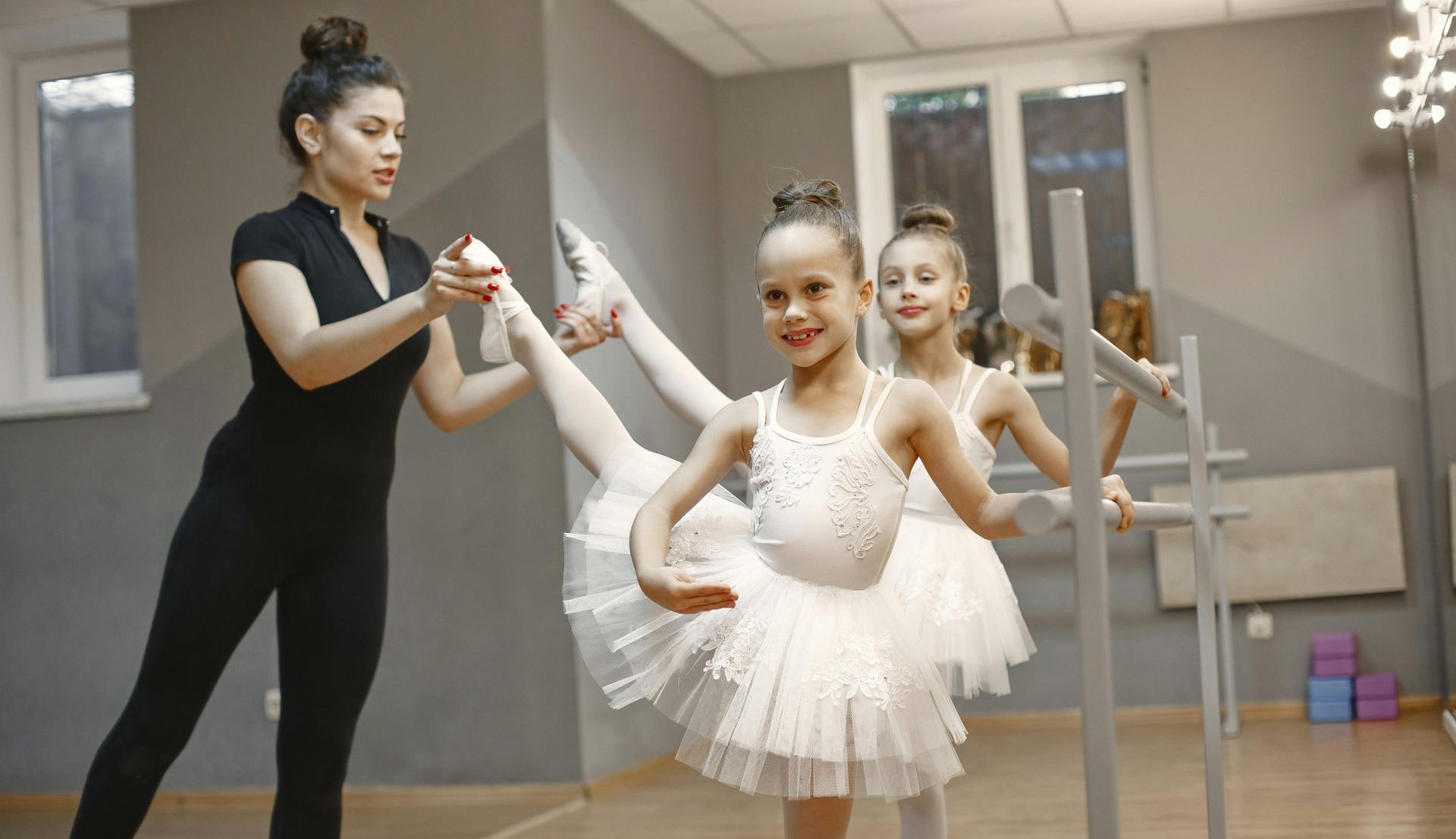 A woman is teaching two little girls how to dance in a dance studio.