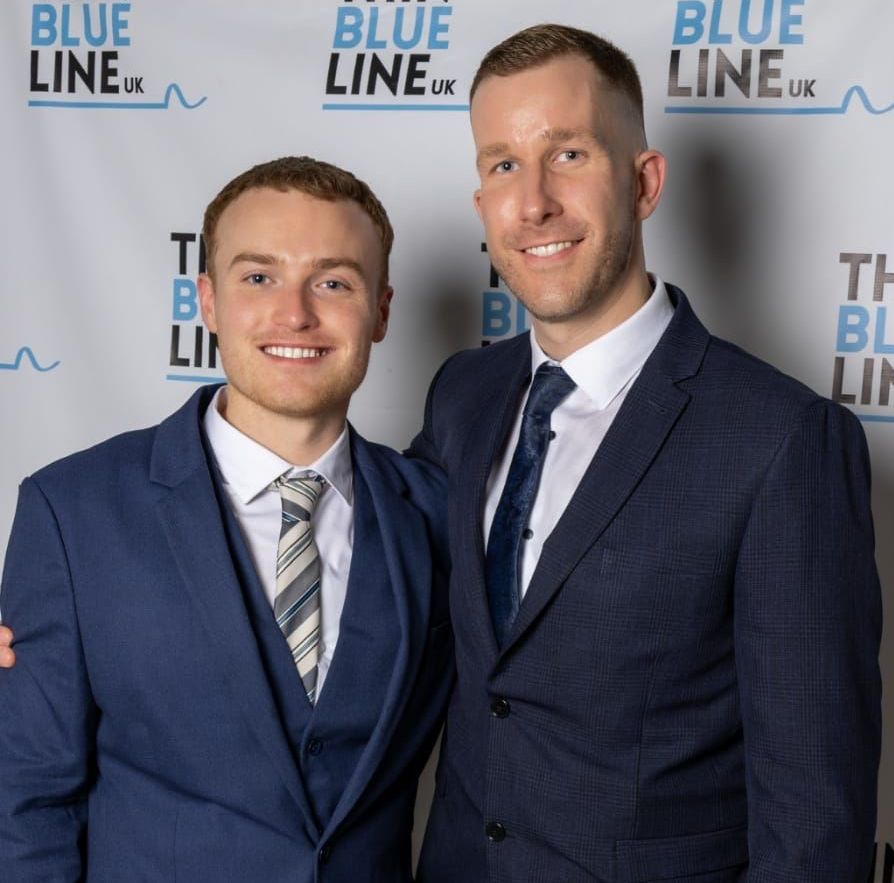 Two men in suits posing for a photo in front of a 