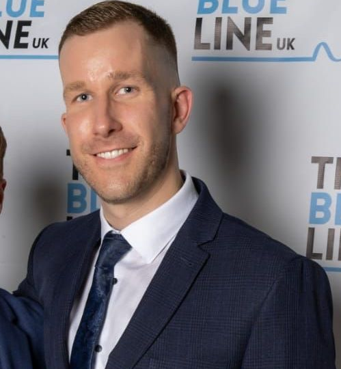 Two men in suits posing for a photo in front of a 