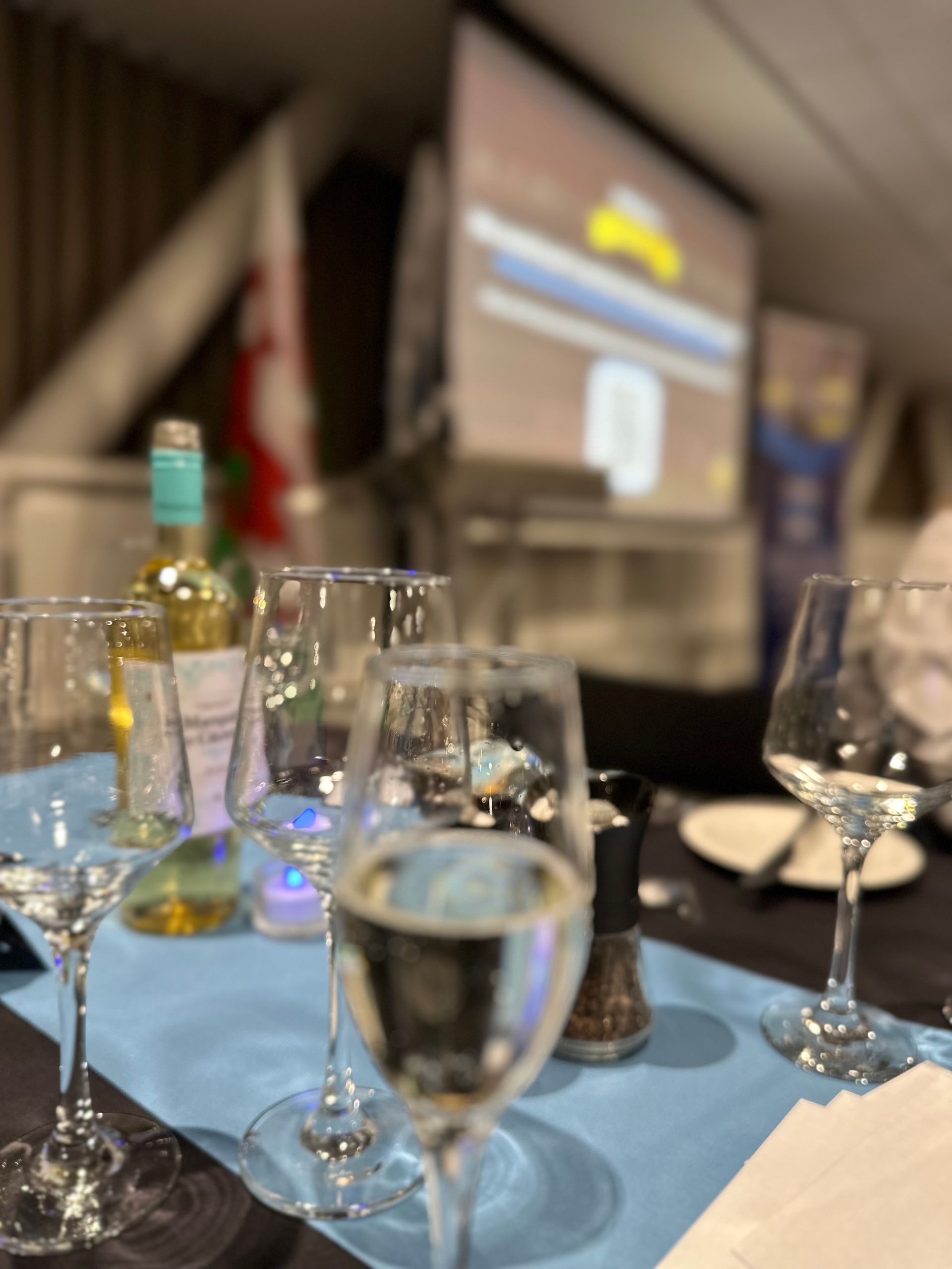Wine glasses on a table set for a gathering, a screen showing a blurred image in the background.