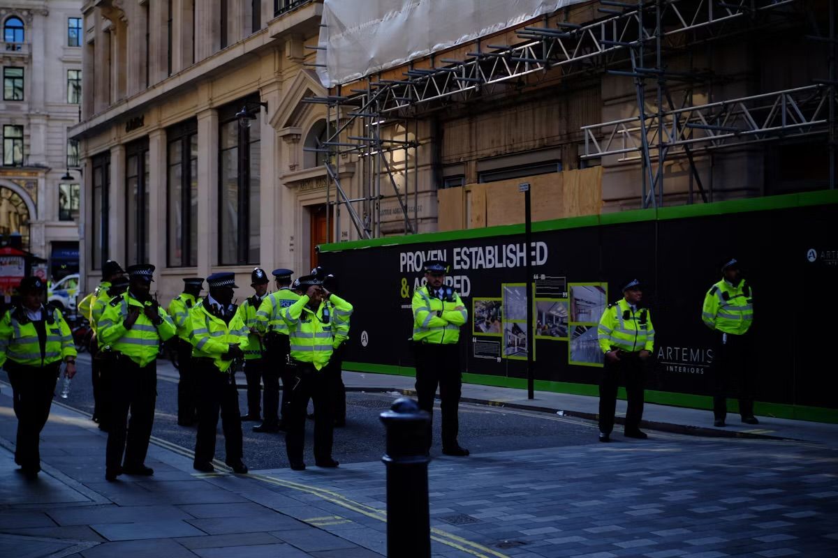 Police officers in neon vests stand on a street in front of a construction site with scaffolding.