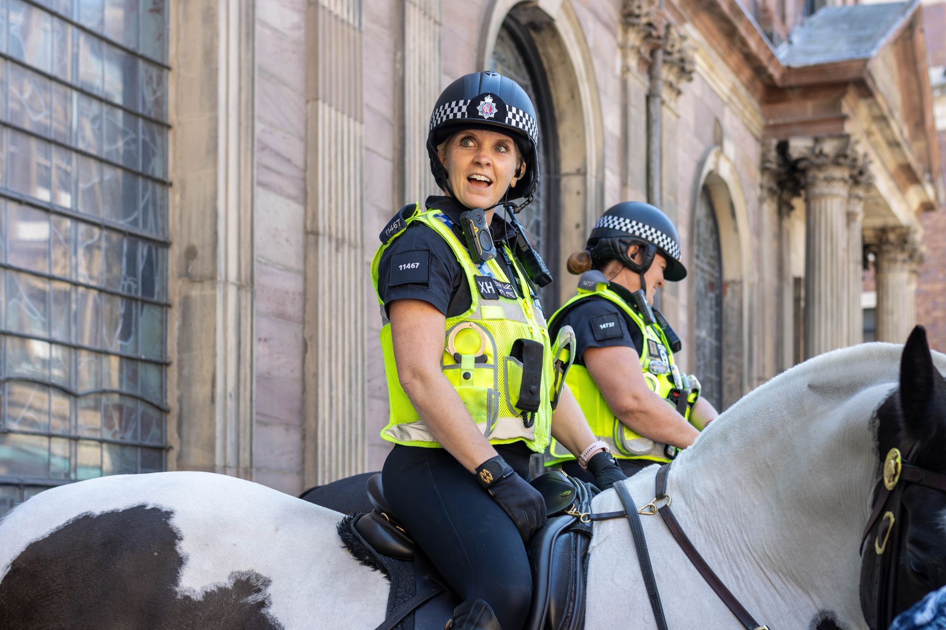 Two mounted police officers in uniform; one looking at the camera. 
