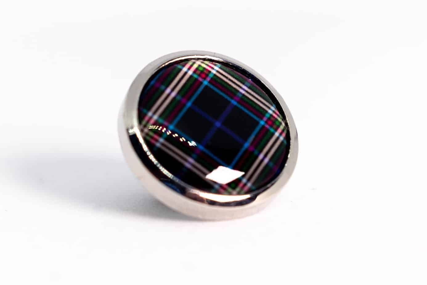 Circular button with a tartan plaid design encased in a silver metal rim.