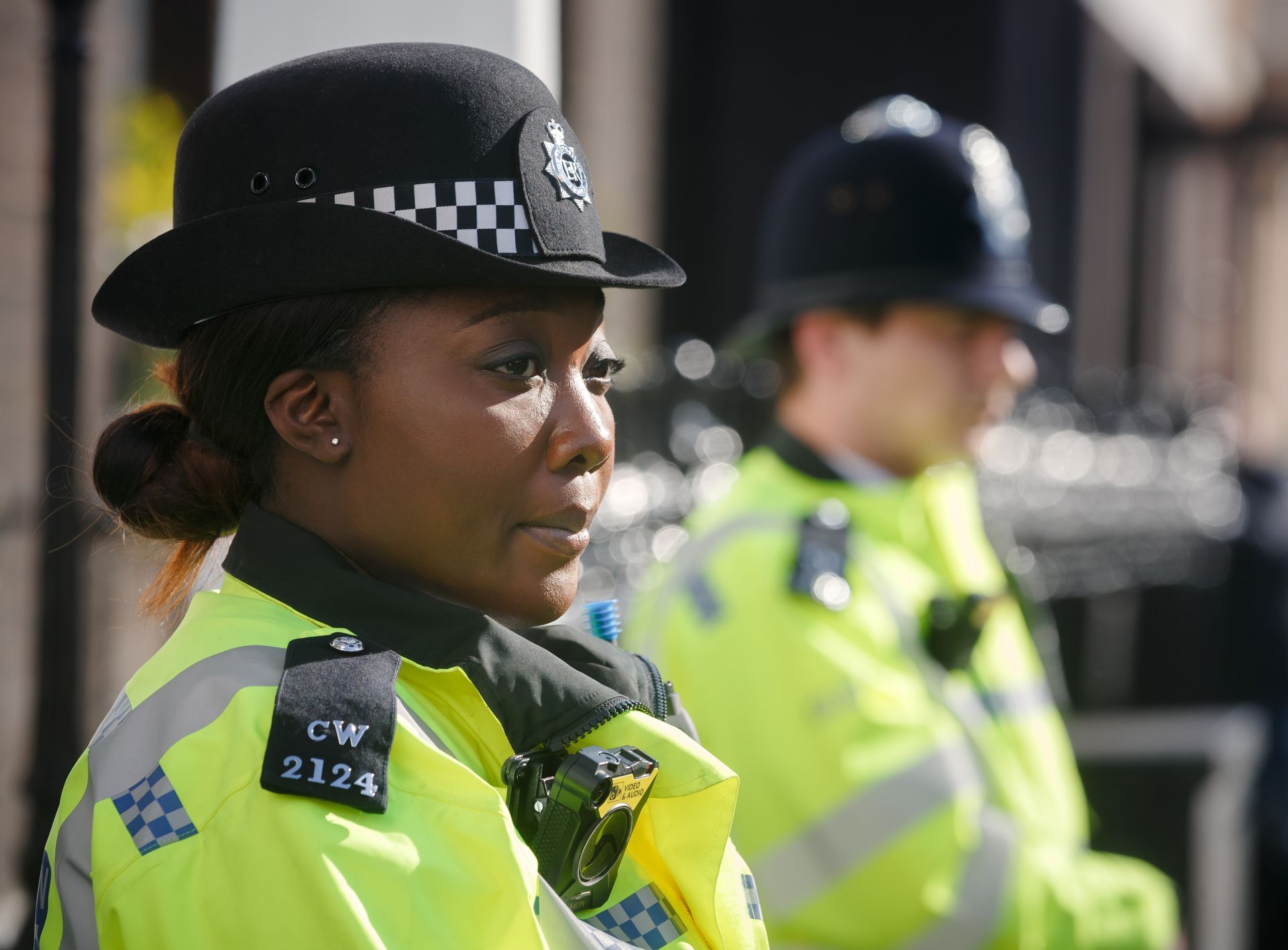 Female police officer in uniform, focused, standing outside with another officer.