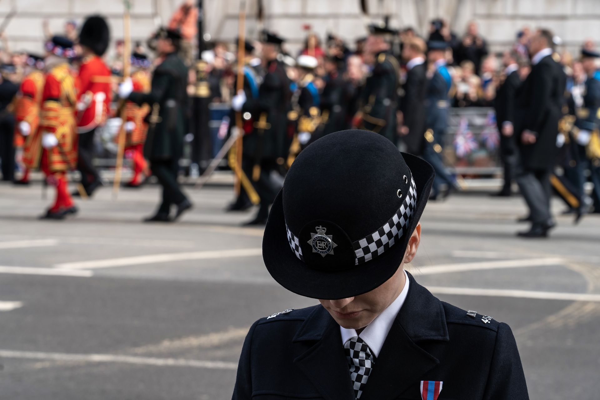 Police officer in uniform at a parade. In the background, soldiers and people in formal attire are visible.