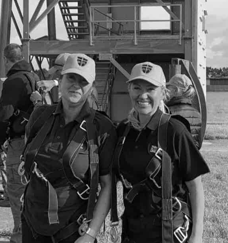 Two women in hats and harnesses pose smiling in front of a tall metal structure.
