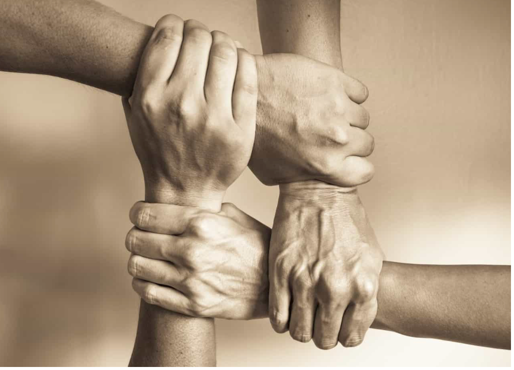 Four hands clasped together, forming a square, symbolizing unity and teamwork.