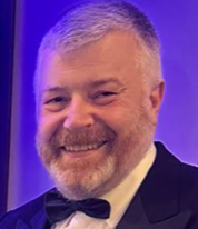 Man with gray hair and beard, wearing a tuxedo, smiling broadly.