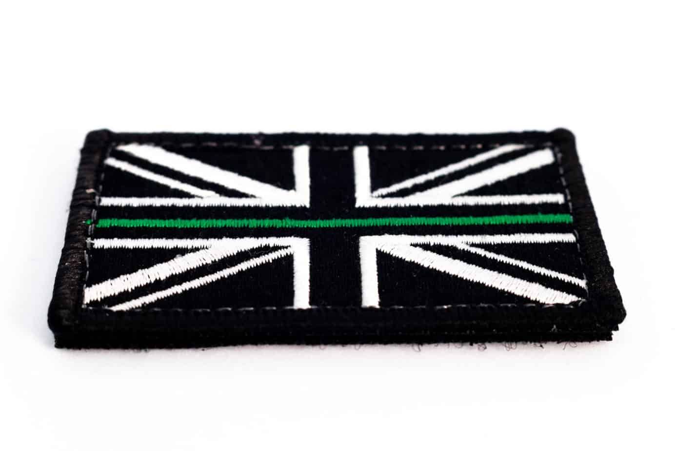 Patch of a black and white Union Jack flag with a green stripe down the middle.