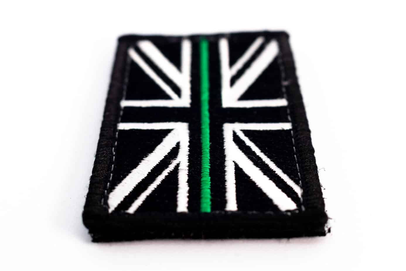 Patch of a black and white Union Jack flag with a green stripe down the middle.