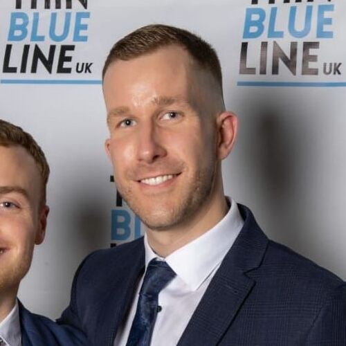 Man in a suit smiles, white shirt, blue tie, at Thin Blue Line UK event.