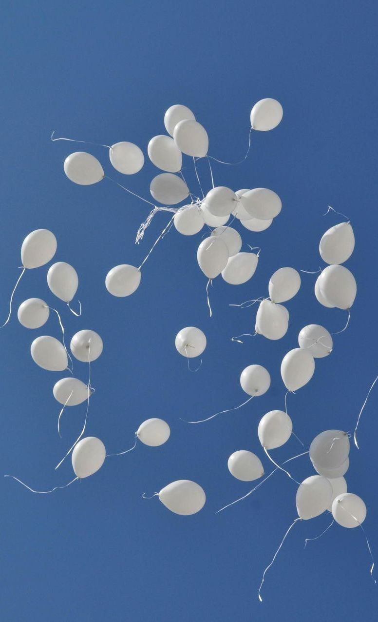 White balloons released into a bright blue sky.