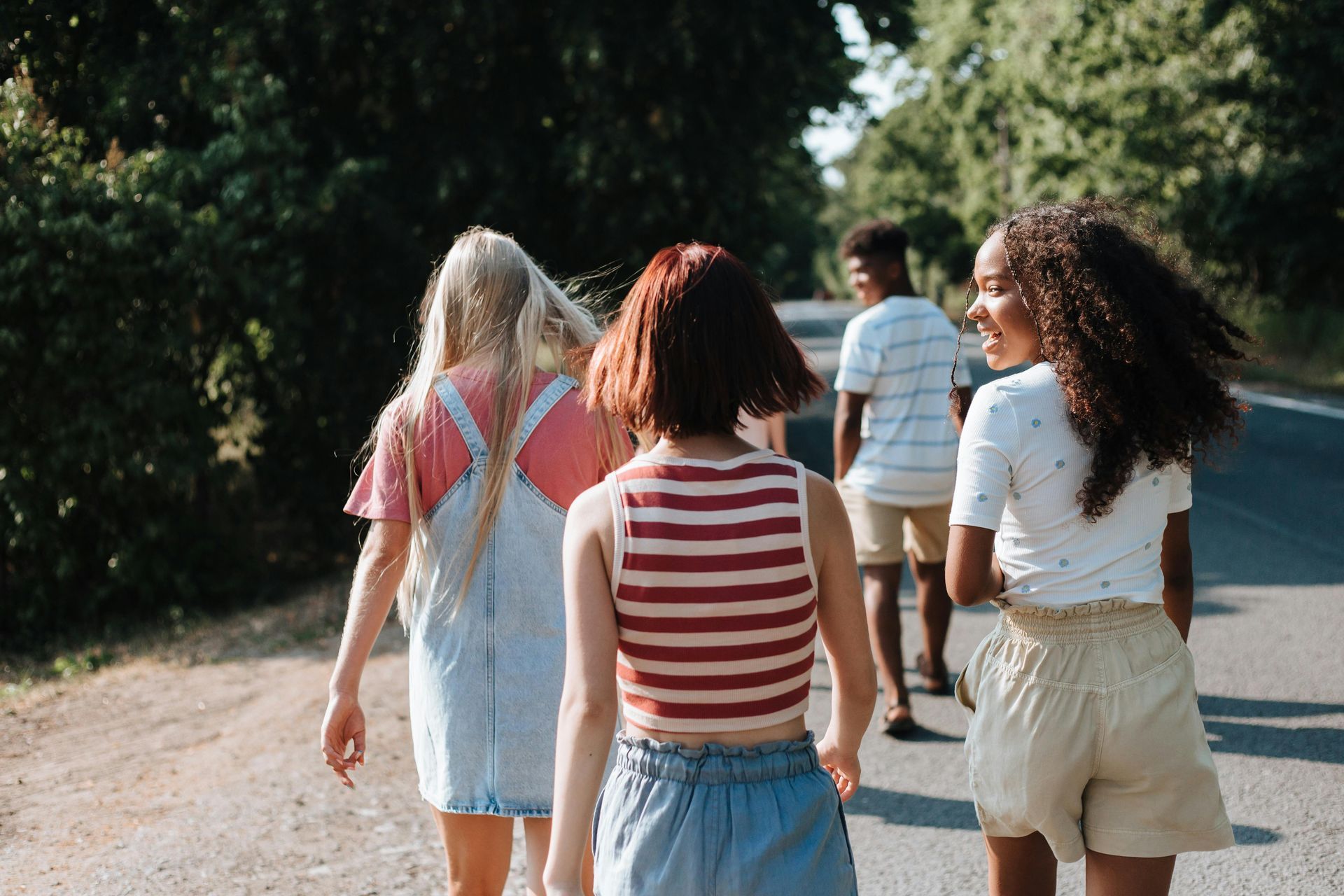 Four young friends walking on a road, smiling, and chatting in sunny weather.