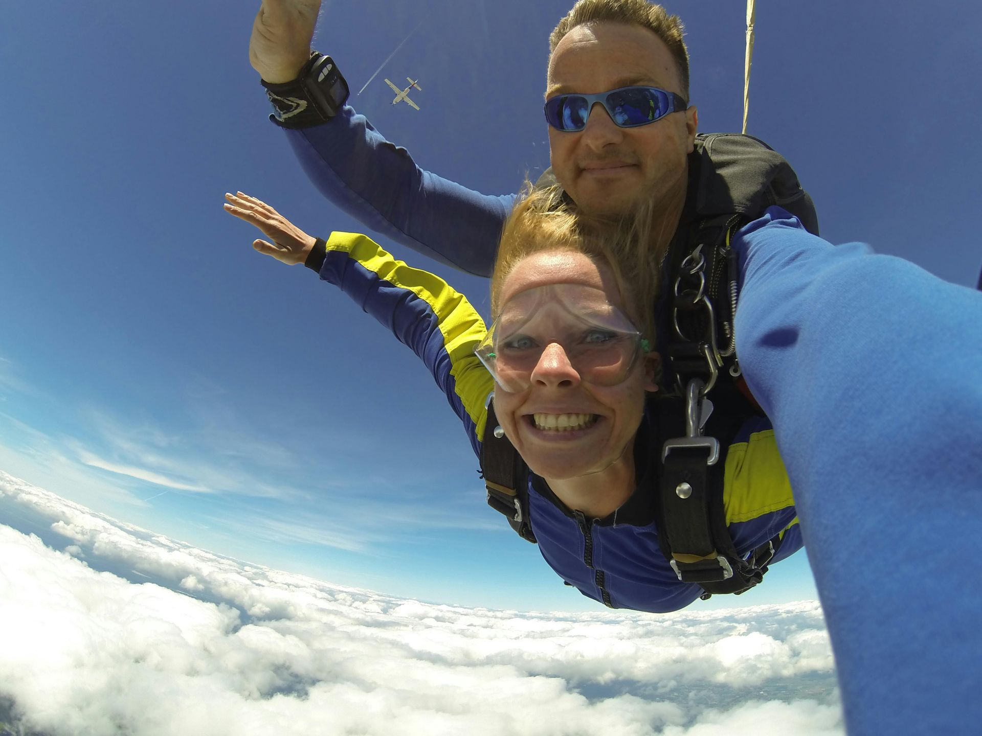 Woman tandem skydiving, smiling with instructor, blue sky and clouds.