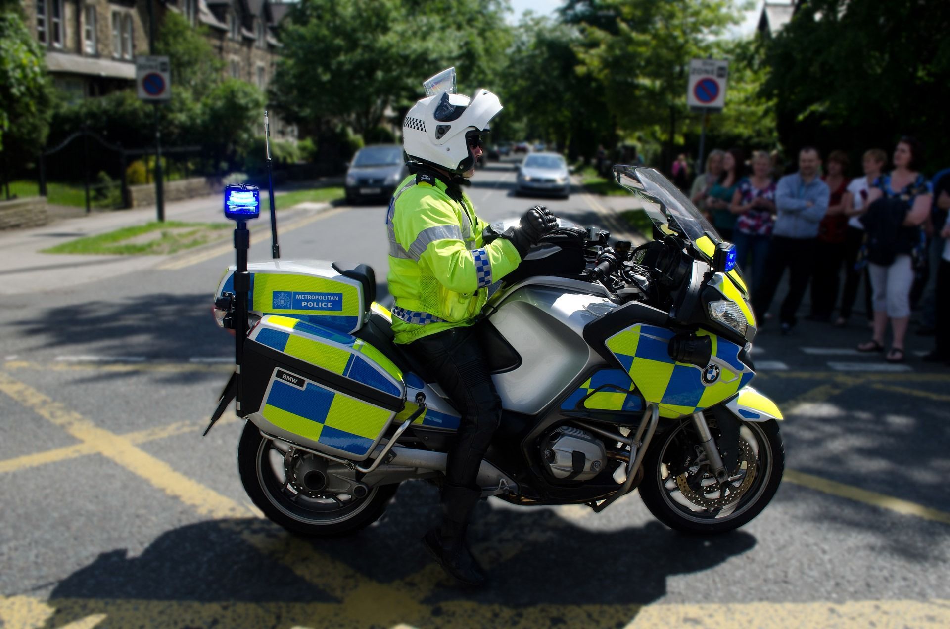 Police officer on motorcycle, wearing fluorescent yellow, blue and yellow checkered markings, on a street.