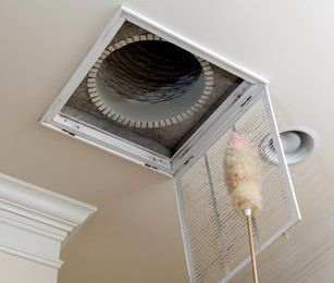 A Person is Cleaning a Ceiling Vent With a Duster