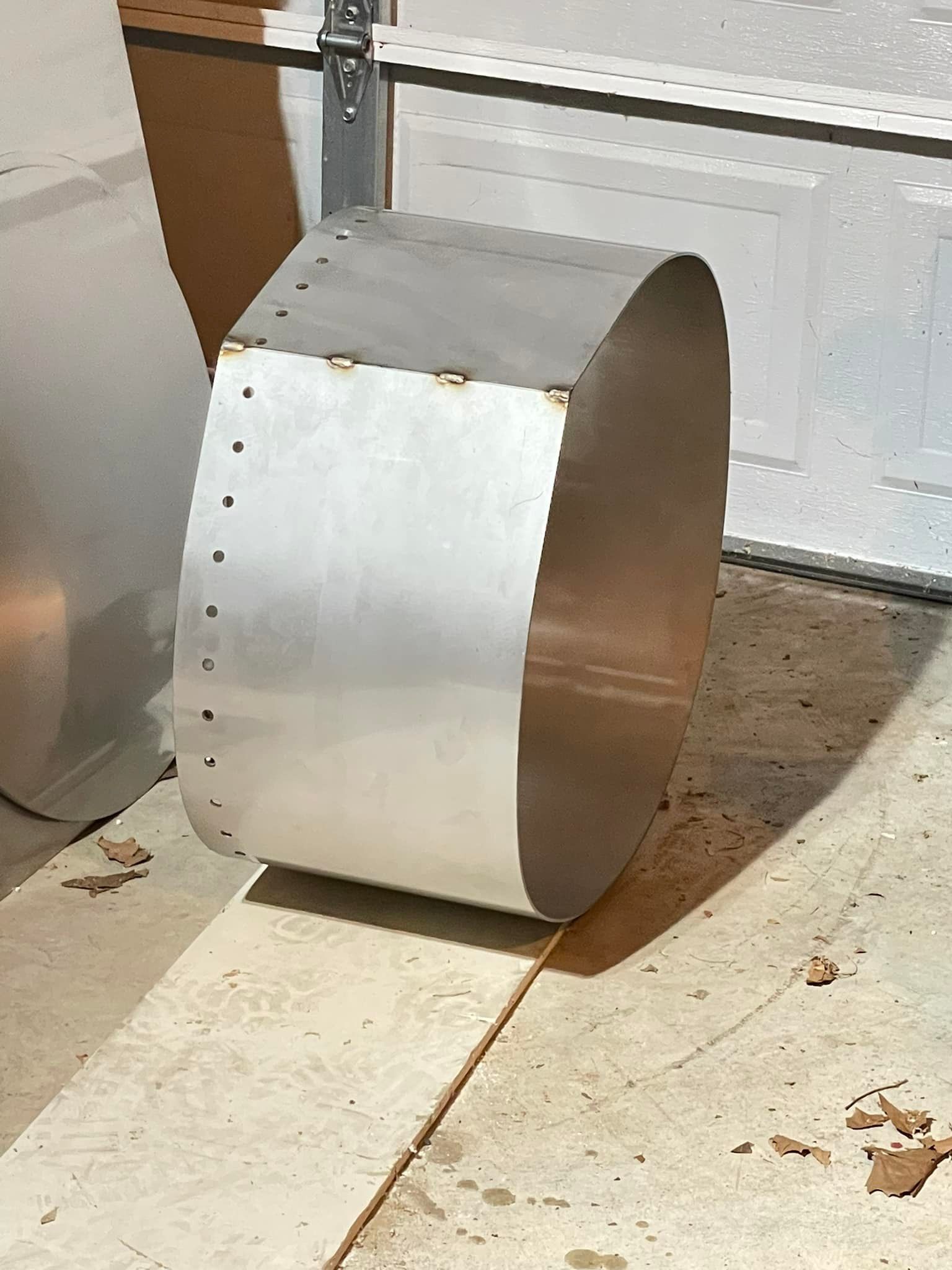 A metal cylinder is sitting on a wooden floor next to a garage door.