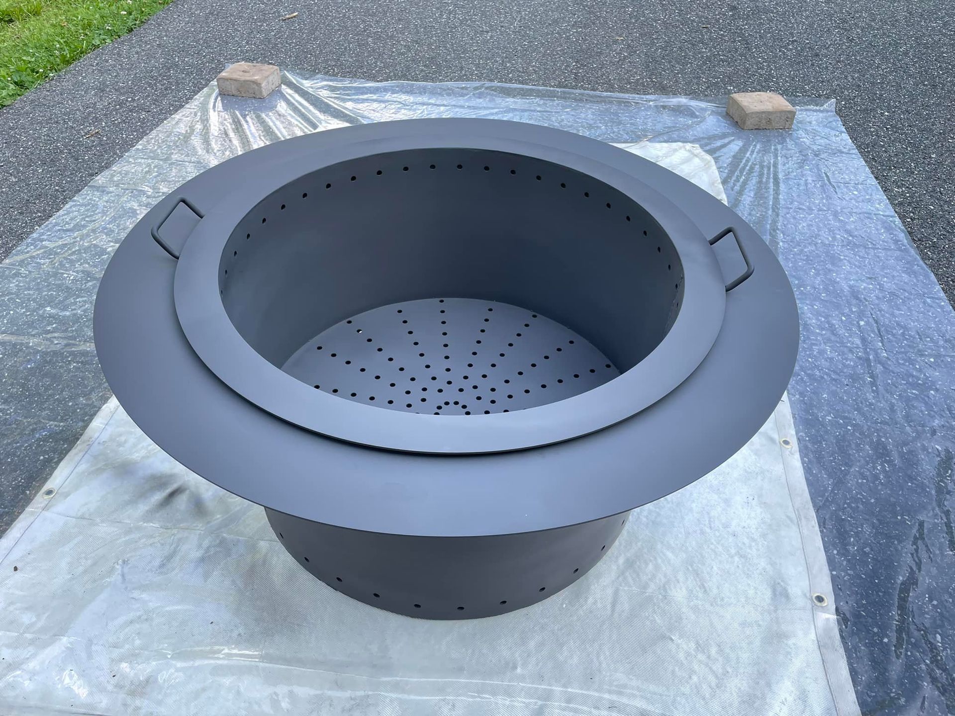 A black fire pit is sitting on top of a plastic tarp