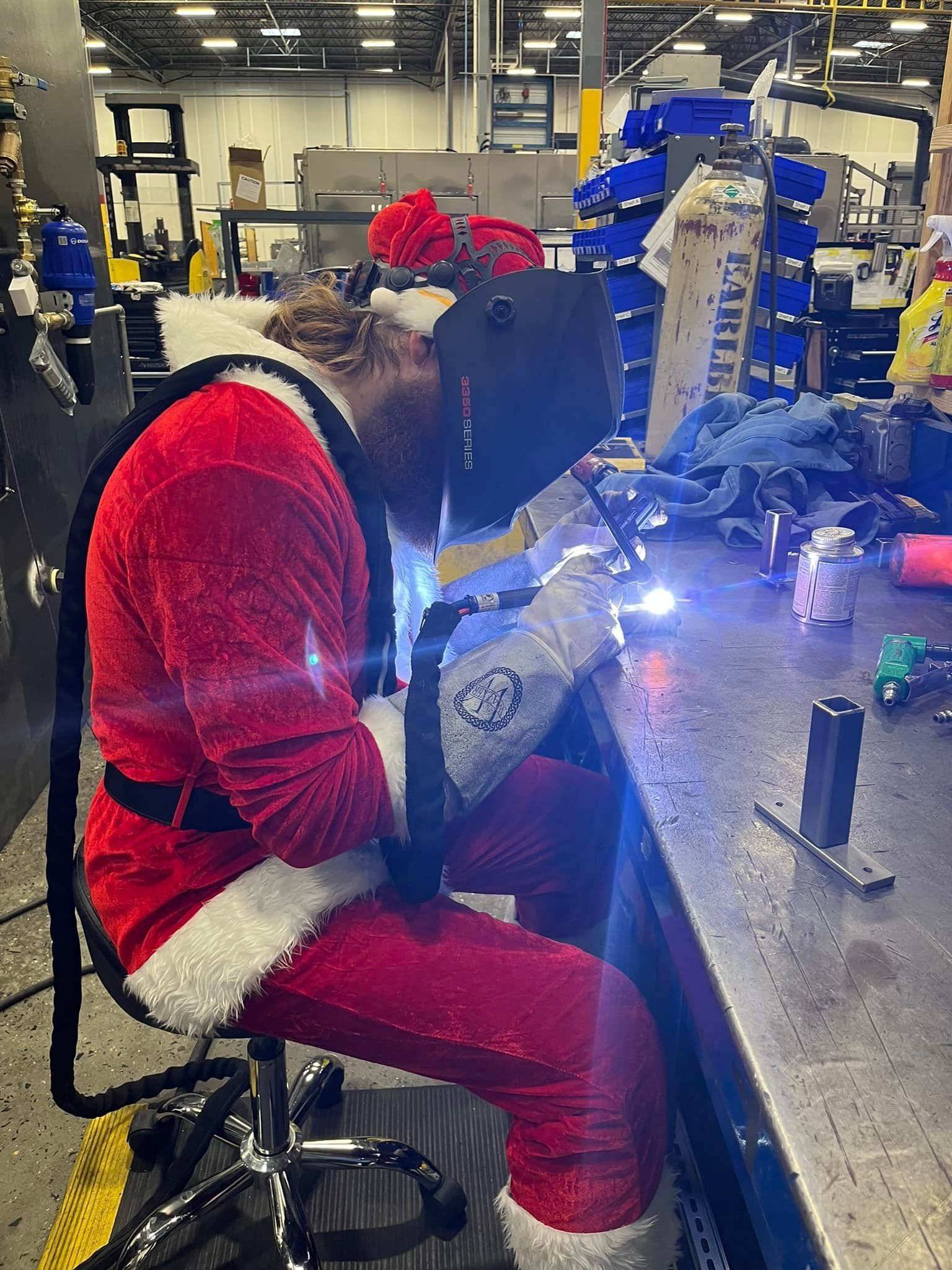 A man dressed as santa claus is welding in a factory.