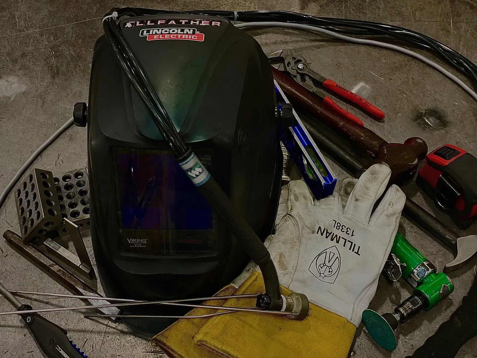 A welding helmet is surrounded by tools and gloves