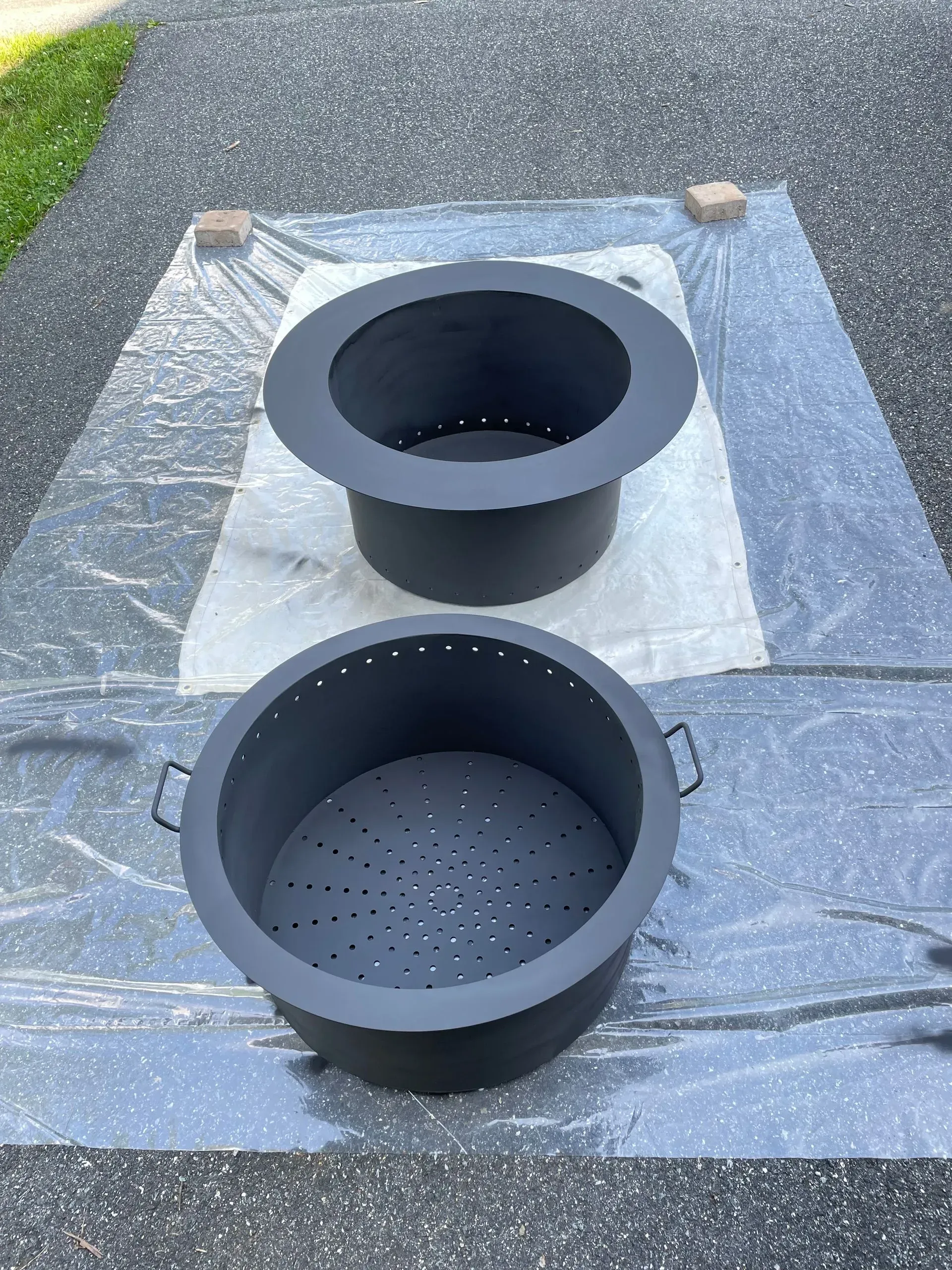 Two black fire pits are sitting on top of a plastic tarp.