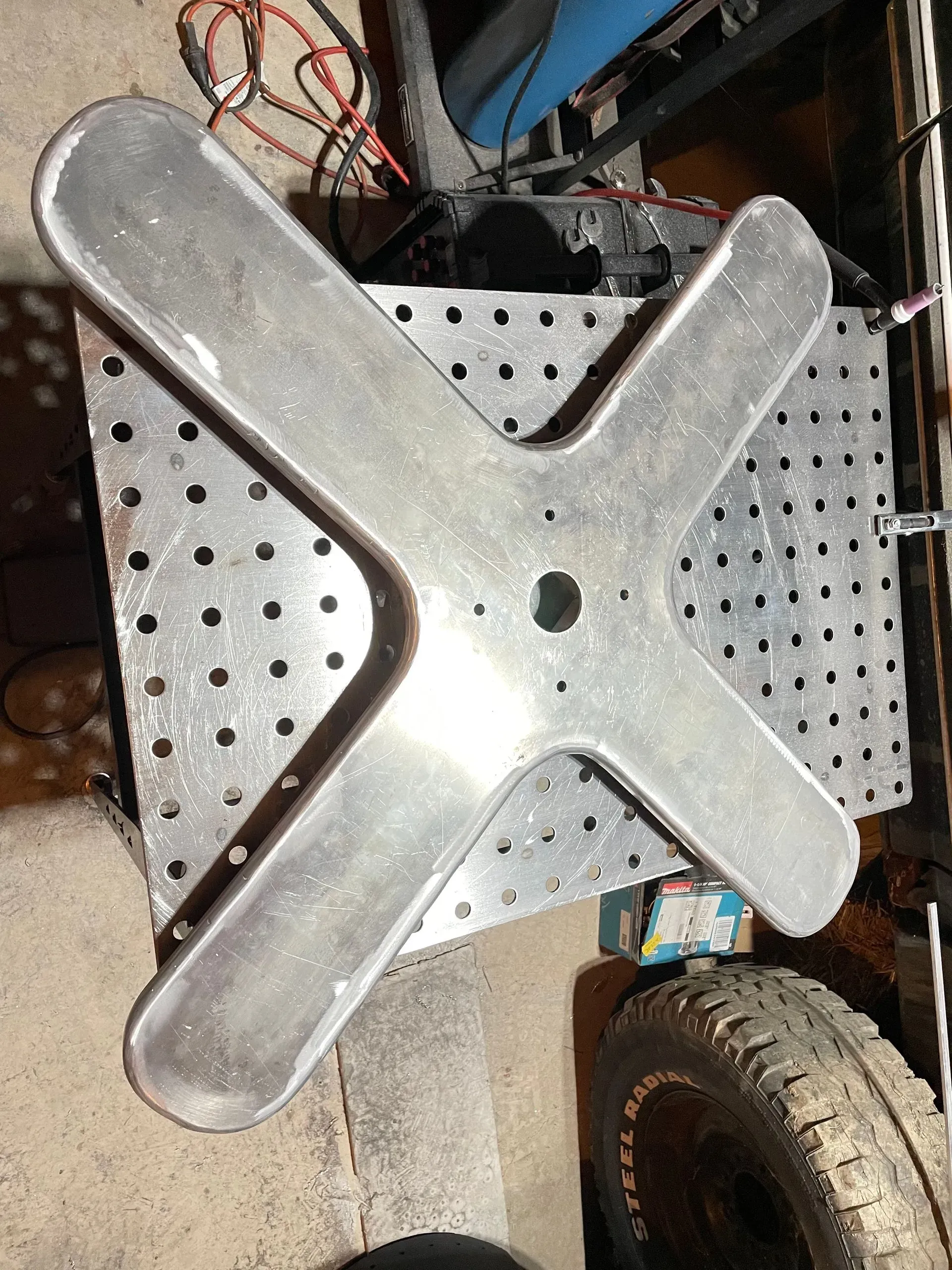 A metal cross is sitting on top of a metal table next to a tire.