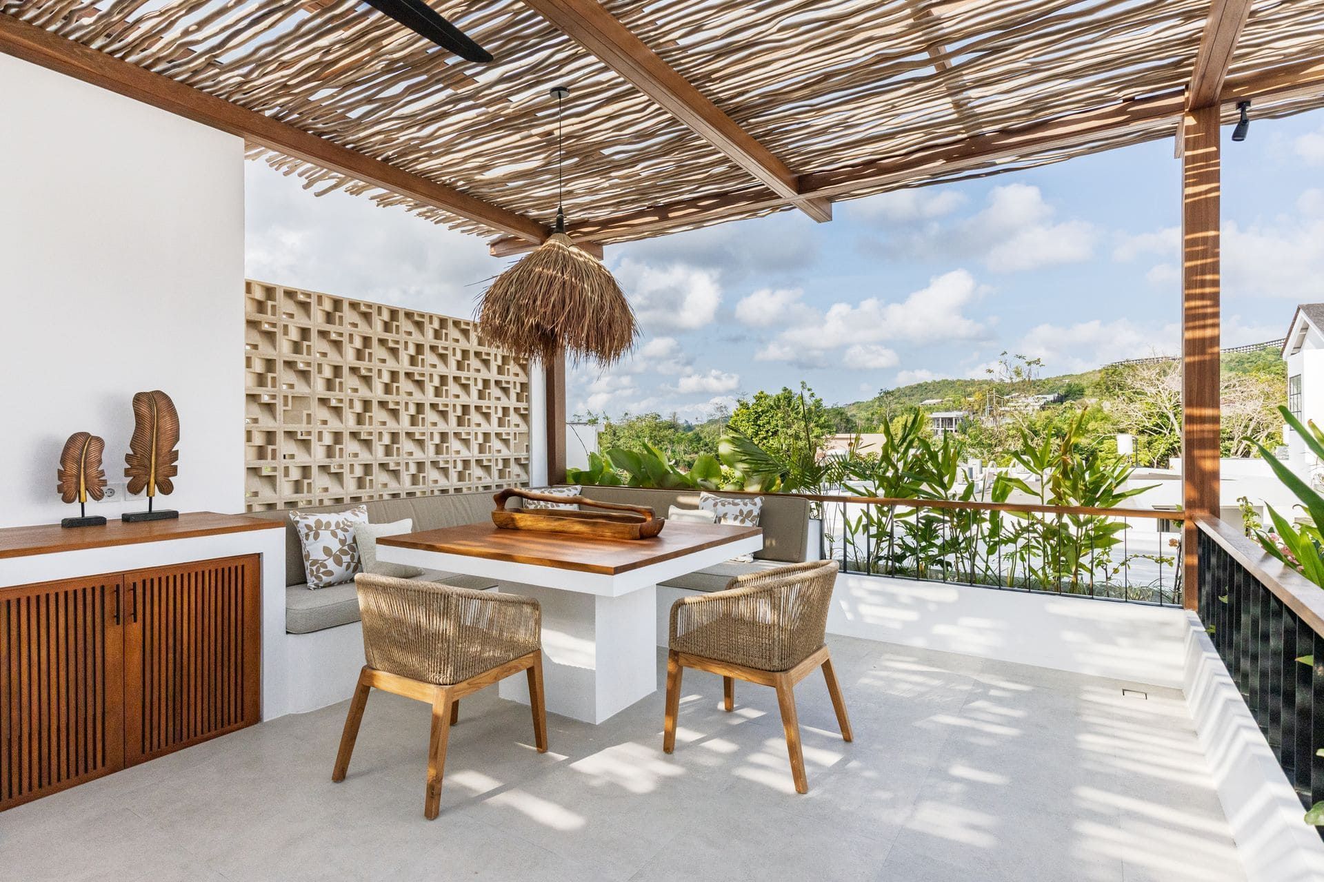 Open-air patio dining area with bamboo roof, wooden table, chairs, and ocean view