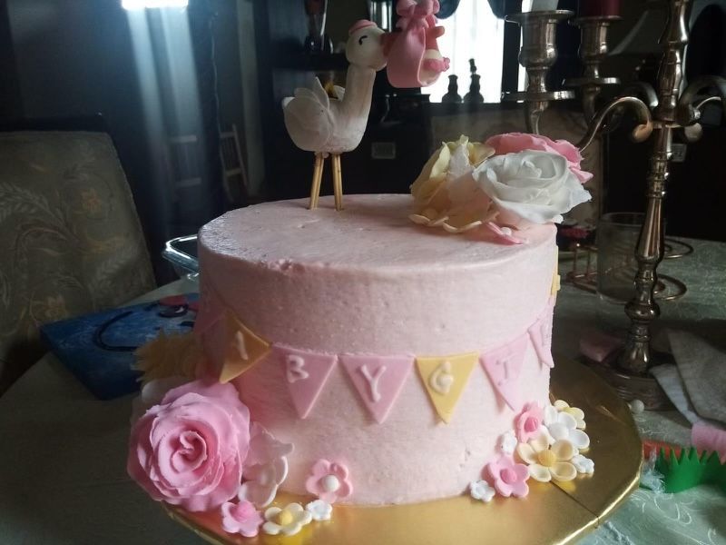 A pink cake with flowers and a stork on top