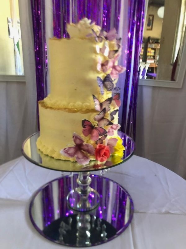 A cake with butterflies on it is sitting on a mirror on a table.