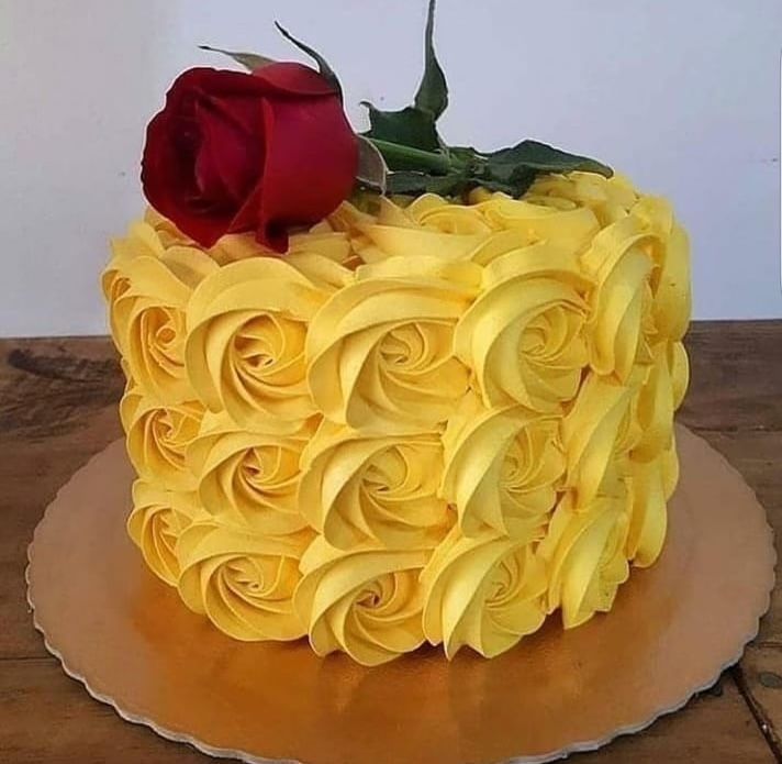 A cake with yellow frosting and a red rose on top