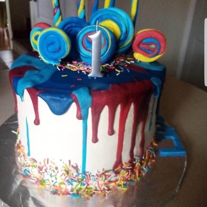 A cake with lollipops and sprinkles has the number 1 on top