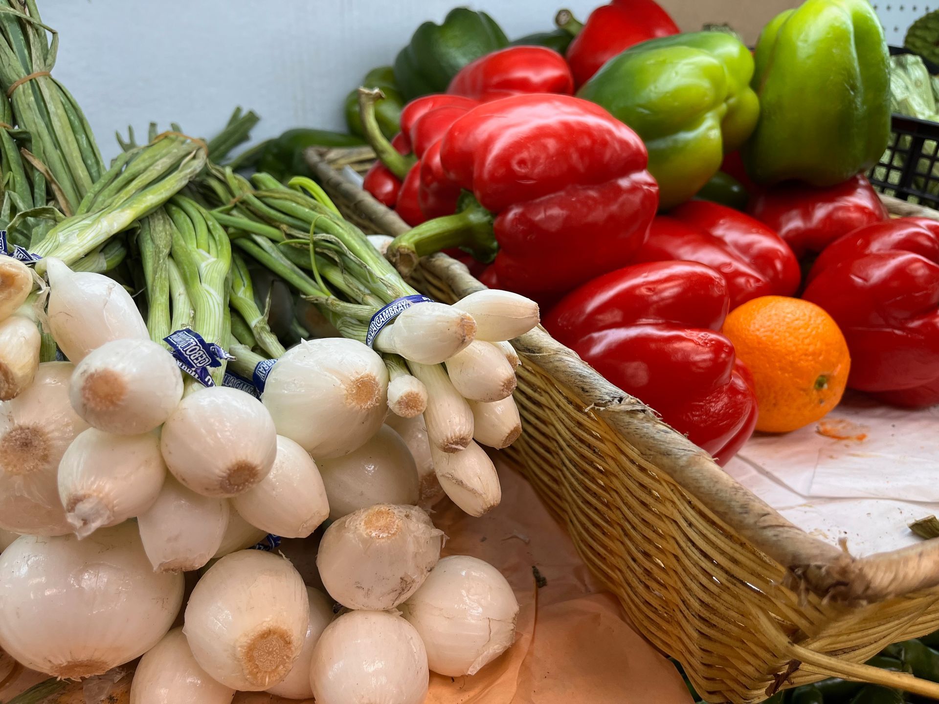 A basket filled with vegetables including peppers onions and oranges