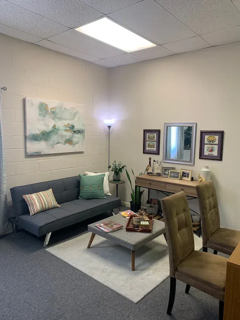 Cozy waiting room with gray sofa, coffee table, and chairs; soft lighting and artwork.