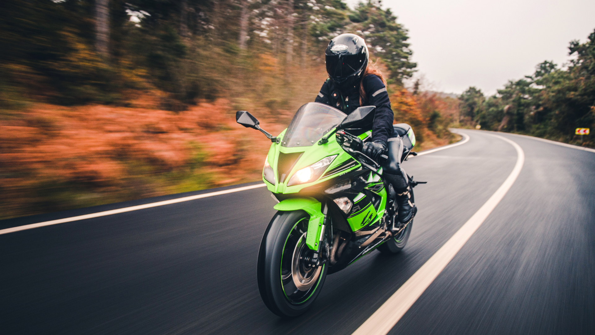 Green Kawasaki motorcycle on a winding road, ridden by a person wearing black protective gear.