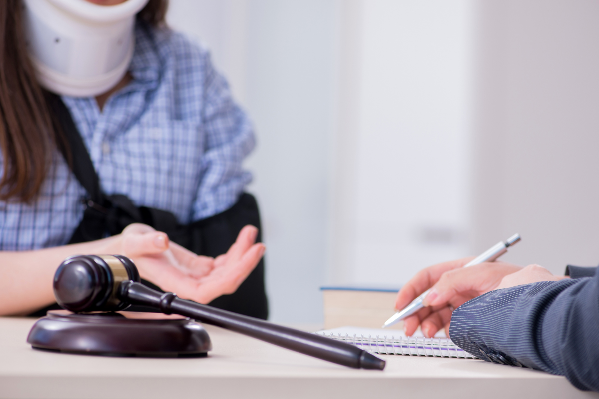 Woman in neck brace and sling meeting with a lawyer, gavel on table.