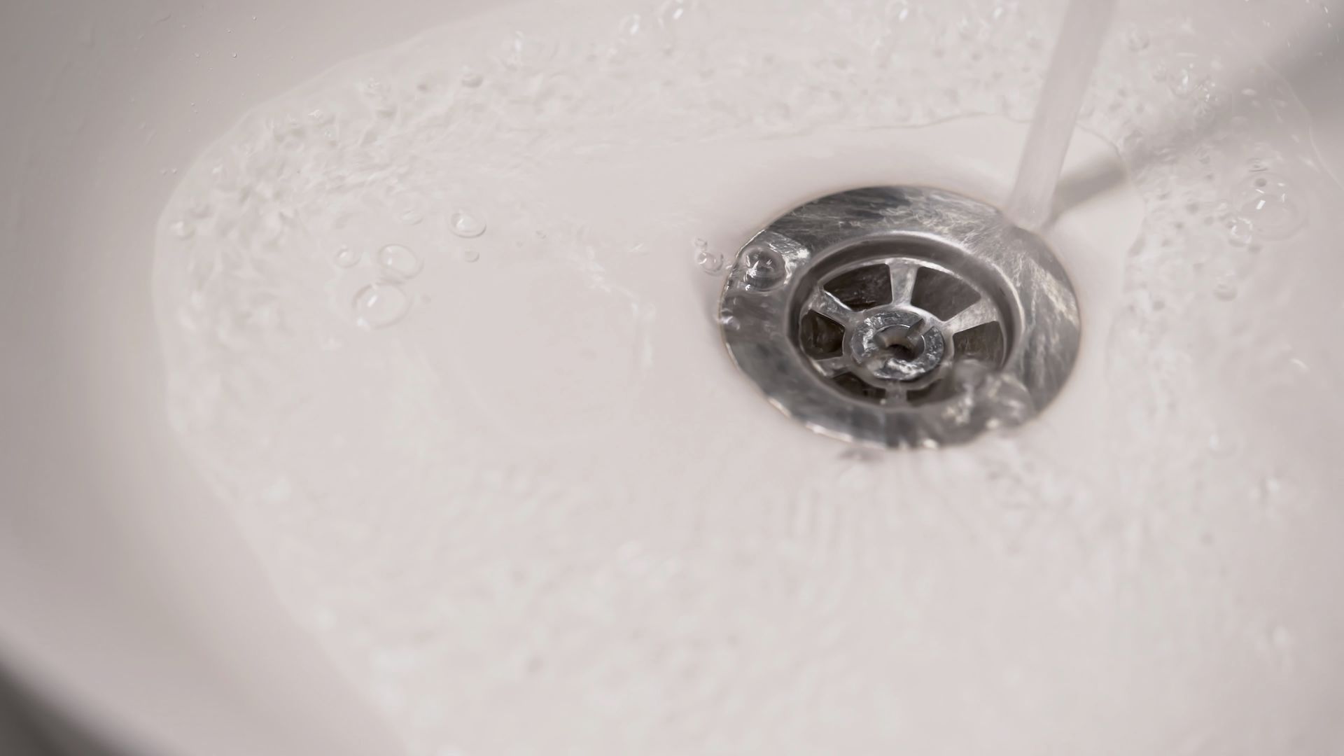 Water is running down a drain in a bathroom sink.