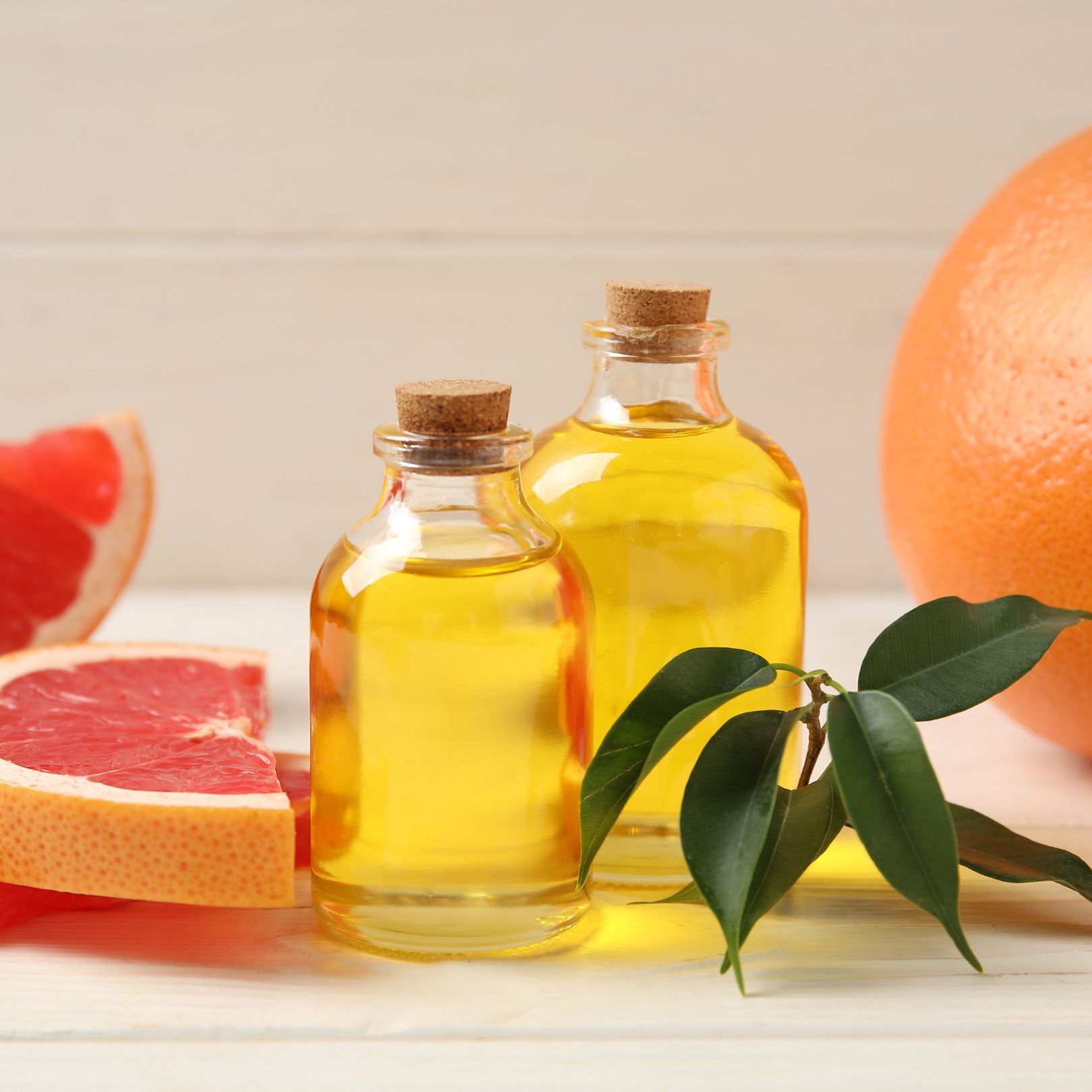 Two glass bottles of yellow oil with grapefruit and leaves.